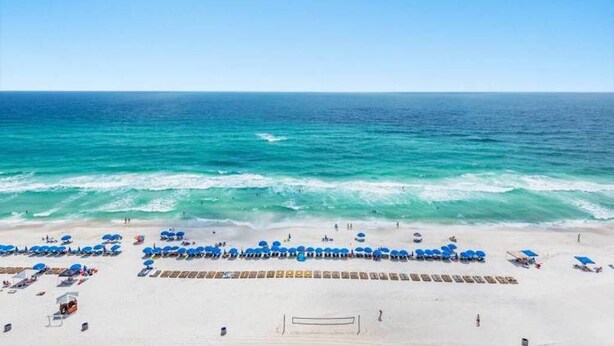 A beach with rows of blue umbrellas and sun loungers, a volleyball net, and the ocean in the background. - Aqua 3br/3ba. 2 Master BD ocean view (Panama City Beach)