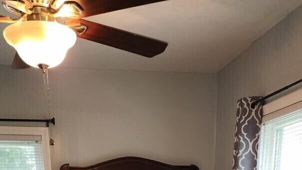 Une chambre avec un grand lit, un ventilateur de plafond, un miroir et une fenêtre avec des rideaux.