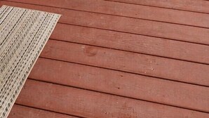Une terrasse en bois avec un paillasson, une table avec un coussin rouge et une porte portant l’inscription « G SUITE ».