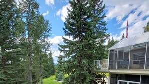 A modern house with a large tree in the front yard, a deck, and a covered outdoor area. - Riverside Retreat - Secluded exotic villa in the Rocky mountains (Waiparous Village)