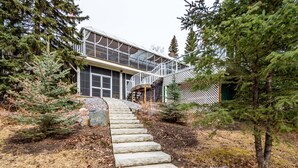 A stone staircase leading to a modern house with large windows and a covered porch. - Riverside Retreat - Secluded exotic villa in the Rocky mountains (Waiparous Village)