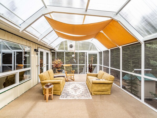 A sunroom with large windows, a wooden ceiling, and a beige carpet.