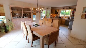 A spacious dining area with a wooden table and wicker chairs, a kitchen with wooden cabinets, and a large window providing natural light.