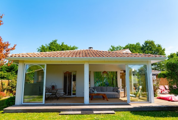 A modern house with a tiled roof, glass doors, and a patio with outdoor furniture. - Very comfortable villa with heated pool between ocean, bay and lake (Le Porge)