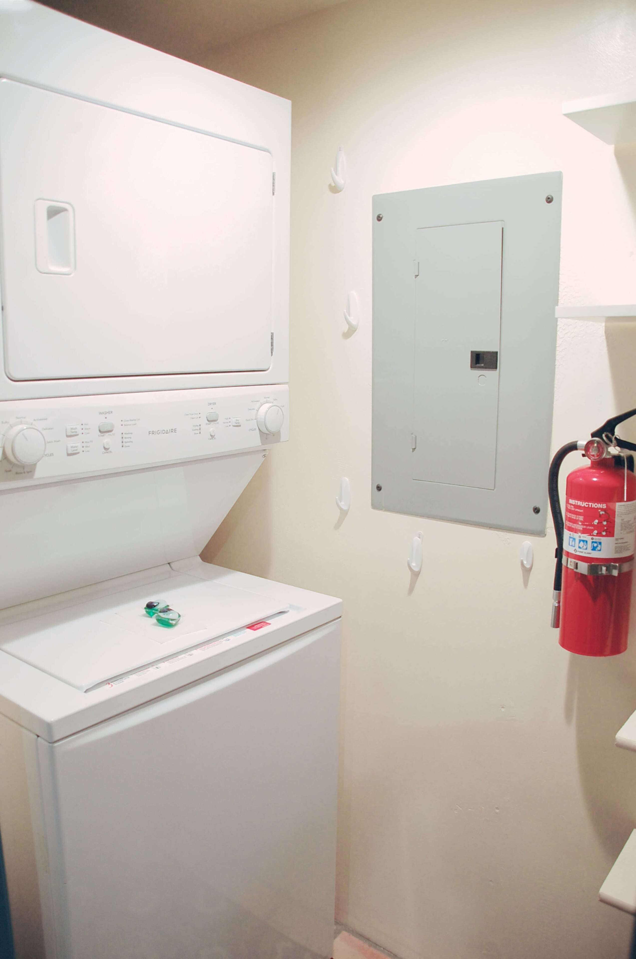 A laundry room with a washing machine, dryer, and a fire extinguisher mounted on the wall.