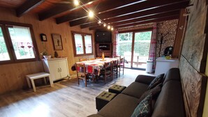 A cozy room with a wooden ceiling, a sofa, a dining table with chairs, a bench, and a TV. - Chalet de l'écureuil, petanque ground in the Vosges mountains near Gérardmer and Alsace (Anould)