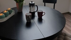 Pyöreä pöytä, jonka päällä on kahvinkeitin, kaksi mukea, tulppaanimaljakko ja pieni kasvi.