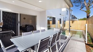 En terrasse med spisebord og stole, grill og en skydedør, der fører til en opholdsstue.