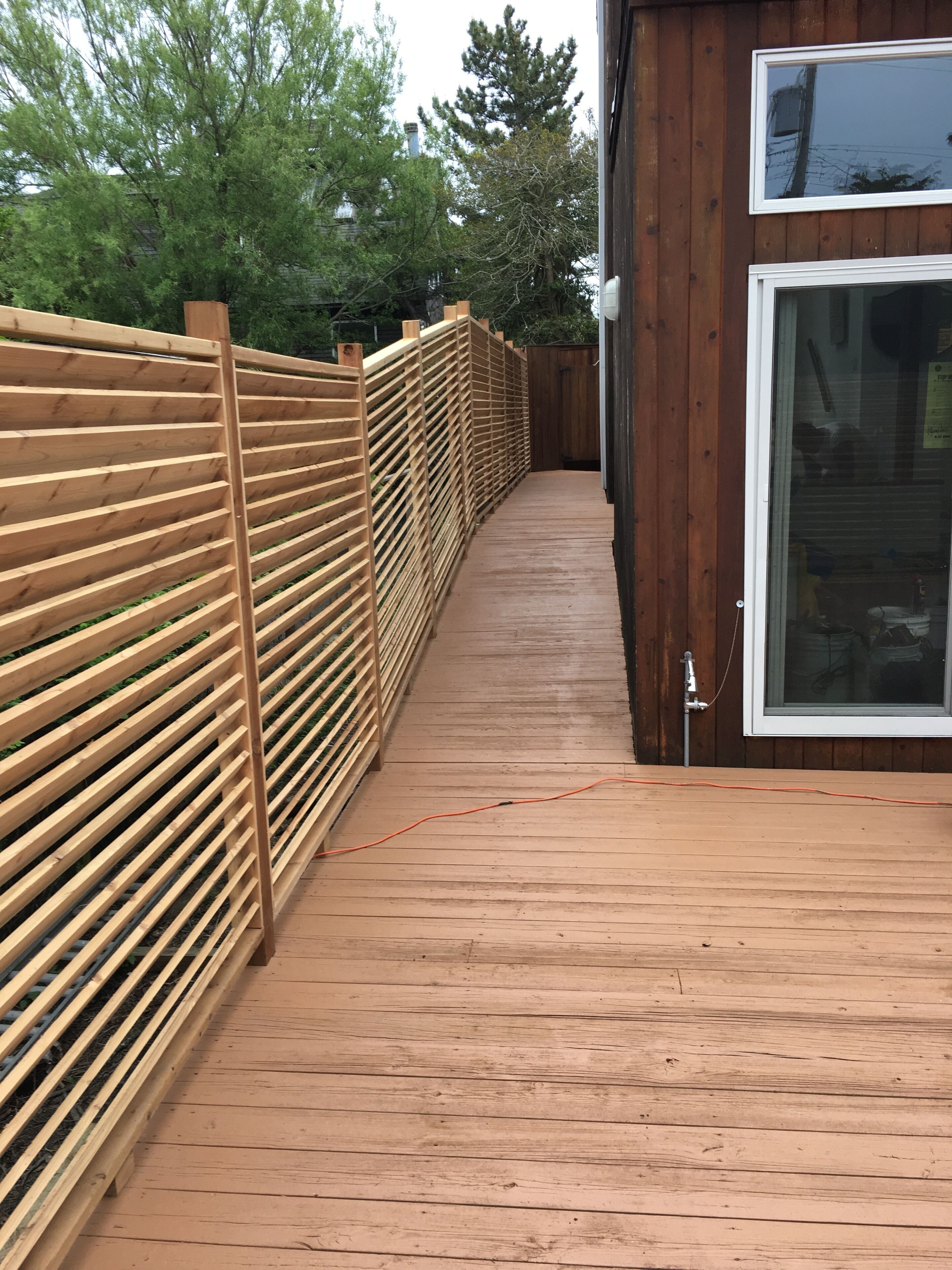 A wooden deck with a metal railing, leading to a building with a large window.
