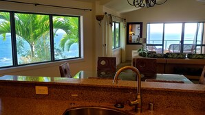 A kitchen with granite countertops, a stainless steel sink, and a view of the ocean through large windows.