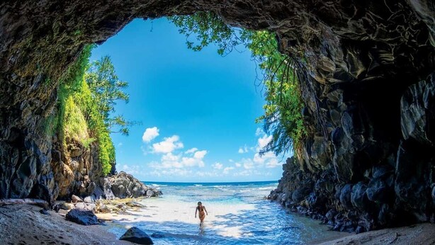 A beach scene with a person walking towards the water, framed by a cave entrance.