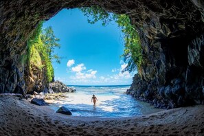 A beach scene with a person walking towards the water, framed by a cave entrance.