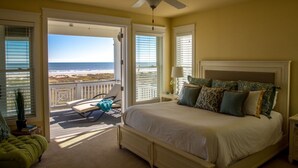 Ein Schlafzimmer mit einem großen Bett, einem Deckenventilator und Blick auf den Strand durch offene Türen.