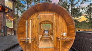 Una cabaña de madera con interior circular, una terraza de madera afuera y vistas a árboles y cielo.