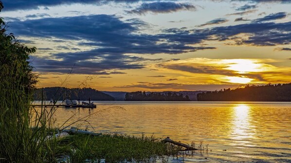 Ein friedlicher See bei Sonnenuntergang, mit Booten auf dem Wasser und einem bewaldeten Hügel im Hintergrund.