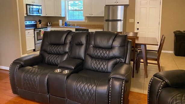 A modern kitchen with white cabinets, a stainless steel refrigerator, and a dining area with a table and chairs. - Bring Your Boat, Pets and Adventurous Spirit- Located Near It All (Guntersville)