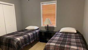 A bedroom with two single beds, a nightstand with a lamp, a window with blinds, and a door. - Bring Your Boat, Pets and Adventurous Spirit- Located Near It All (Guntersville)