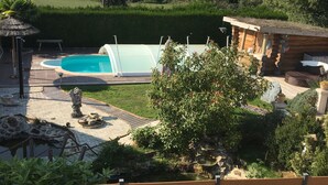A backyard with a swimming pool, a wooden deck, and a small wooden cabin.