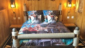 A wooden-themed bedroom with a bed featuring a pirate-themed bedspread and matching pillows.