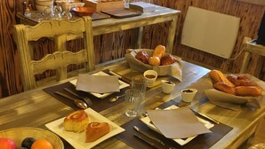 A wooden dining table with a plate of fruit, a basket of bread, and a bowl of pastries.
