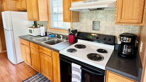 A compact kitchen with wooden cabinets, a white stove, a sink, and a refrigerator. - Walking Distance to Lake James: Private Resort Amenities  (Marion)