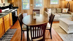 A cozy kitchen with wooden paneling, a dining table with chairs, a ceiling fan, and a view through the windows. - Walking Distance to Lake James: Private Resort Amenities  (Marion)
