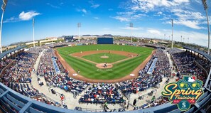Un estadio de béisbol con varios niveles de asientos, un amplio campo de juego y un marcador.