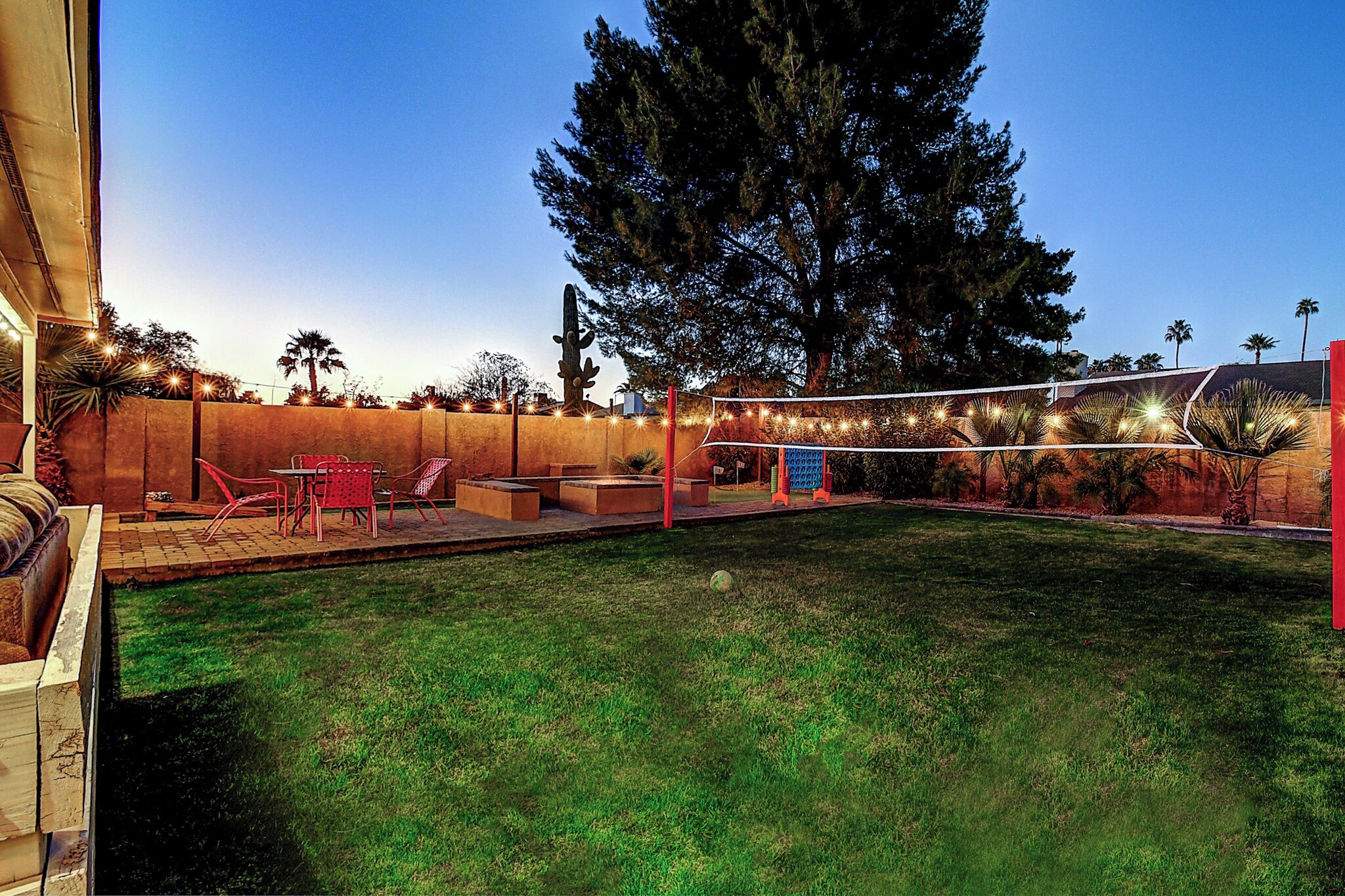 A backyard with a pool, red chairs, and string lights.