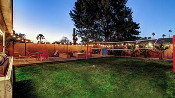A backyard with a pool, red chairs, and string lights.