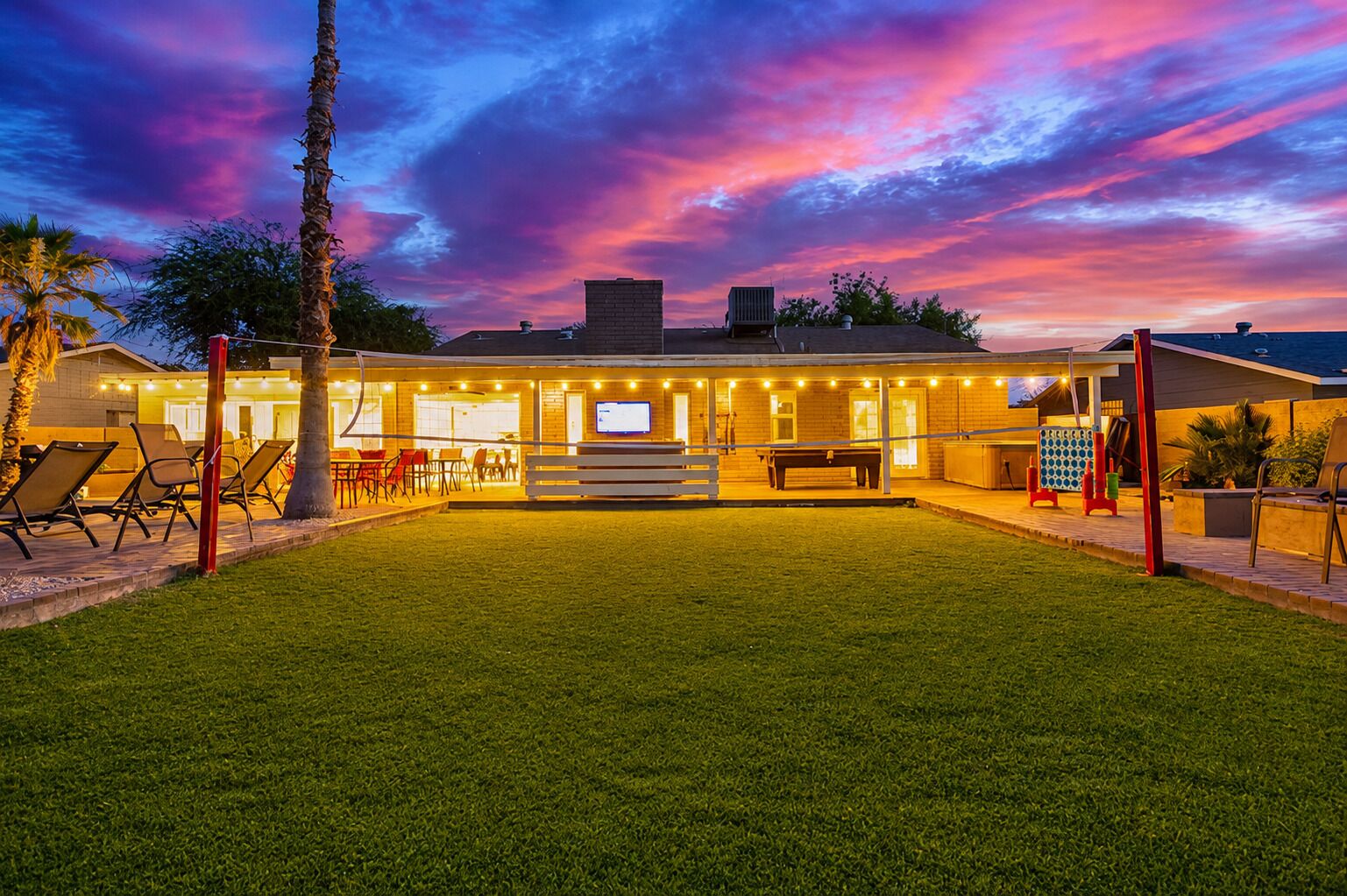 Un patio exterior bien iluminado con mesa de billar, asientos y una pantalla de televisión.