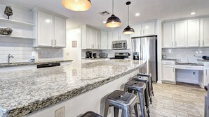 Eine moderne Küche mit weißen Schränken, Granit Arbeitsplatten, Edelstahlgeräten und Pendelleuchten.