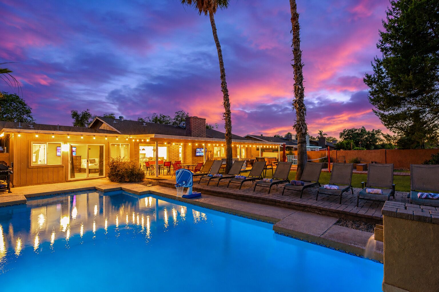 A pool area with lounge chairs and a building with outdoor lighting.