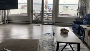 Un soggiorno con televisore, divano, tavolino e vista su un molo e l'acqua.