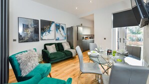 Un salon moderne avec un canapé vert, une table à manger dressée pour quatre personnes et des œuvres d’art accrochées au mur.
