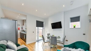 Un salon moderne avec un canapé vert, un fauteuil turquoise et un coin repas comprenant une table et des chaises en verre.