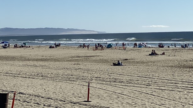 Ein Strand mit Menschen, Zelten und einem klaren Himmel.