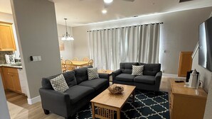 Ein modernes Wohnzimmer mit zwei Sofas, einem Couchtisch, einem Deckenventilator und einem Essbereich im Hintergrund.