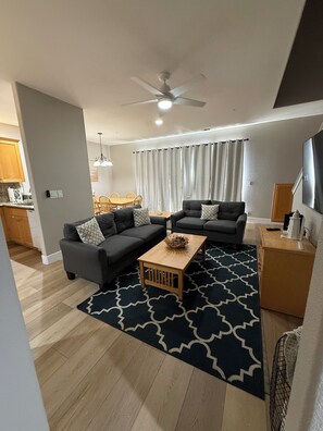 Ein modernes Wohnzimmer mit zwei Sofas, einem Couchtisch, einem Deckenventilator und einem Essbereich im Hintergrund.
