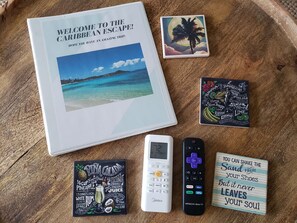 Un guide de voyage, une télécommande, un thermomètre numérique, une télécommande affichant un message motivant et un dessous de verre avec une recette de boisson.