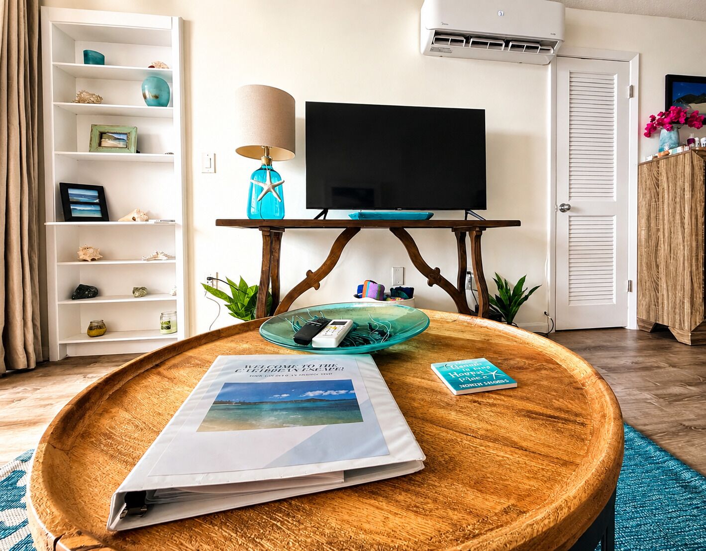 Una sala de estar con una mesa de centro de madera, un televisor sobre un mueble bajo, una estantería y una puerta.