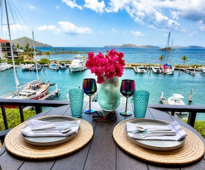 A table set with plates, cutlery, and glasses, overlooking a marina with boats and a clear sky. - Updated: Luxe Condo steps from Sapphire Beach! (St Thomas)