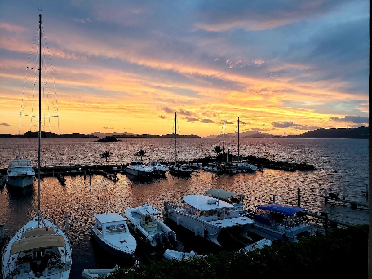 Ein Yachthafen mit an Holzstegen vertäuten Booten, umgeben von ruhigem Wasser und einem Sonnenuntergangshimmel.