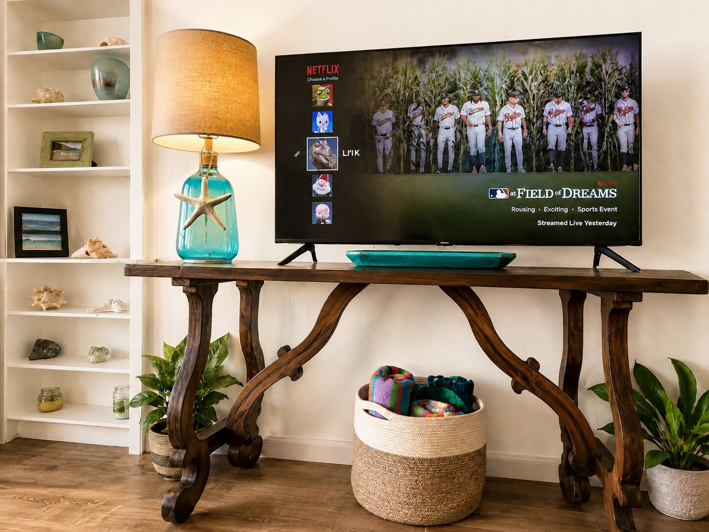 Una televisione su un tavolo di legno, con una lampada, circondata da mensole con oggetti decorativi e piante.