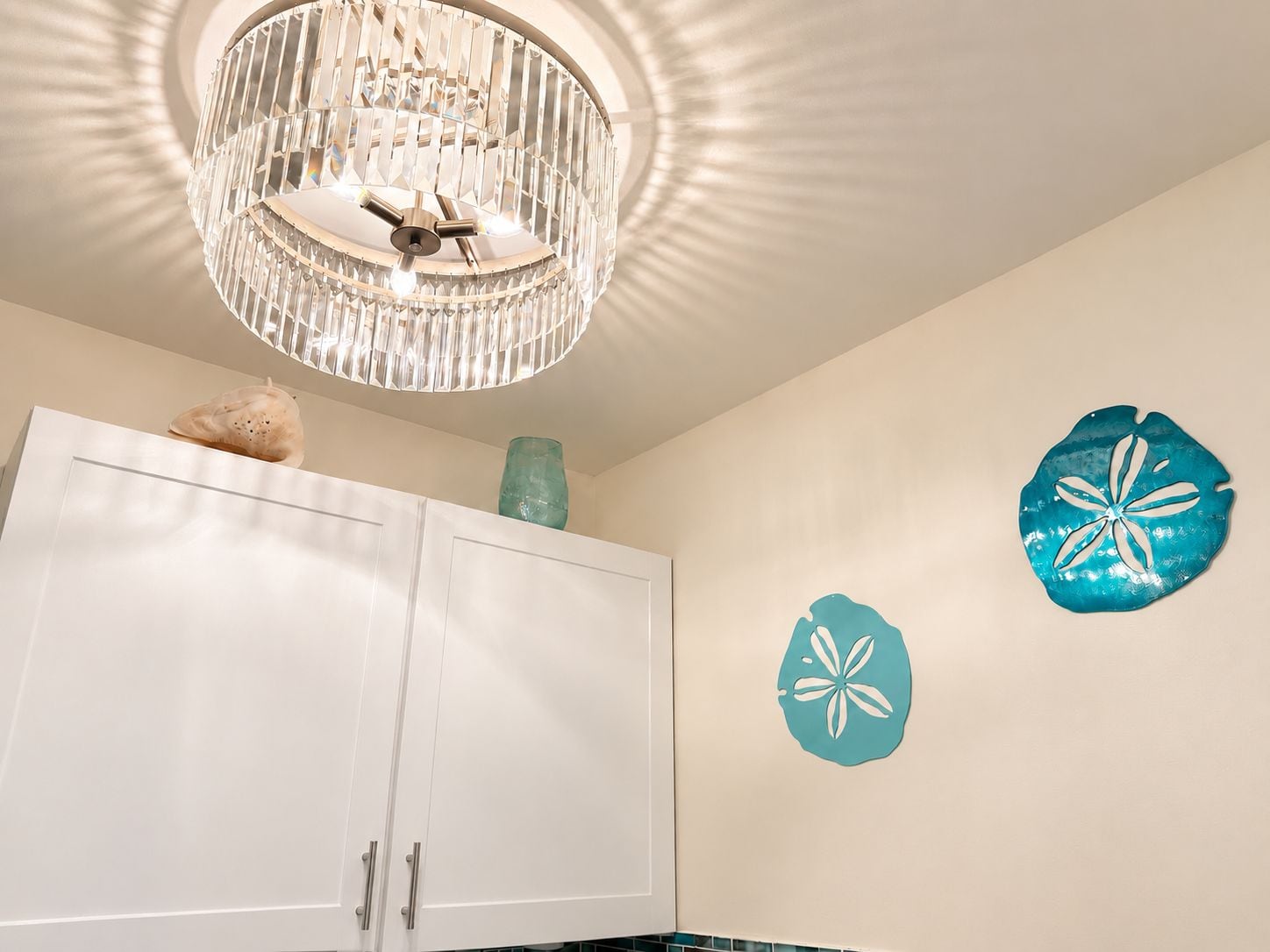 Une cuisine avec des meubles blancs, une assiette décorative de couleur turquoise et un lustre.