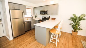A modern kitchen with stainless steel appliances, a white island with bar stools, and a potted plant. - NEWLY RENOVATED SOPHISTICATED INDUSTRIAL TOWN HOME (St. Petersburg)