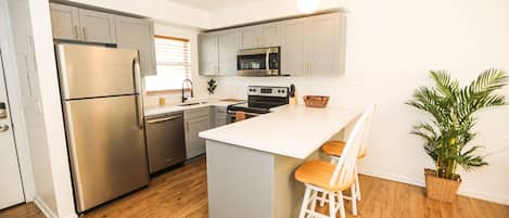 A modern kitchen with stainless steel appliances, a white island with bar stools, and a potted plant.