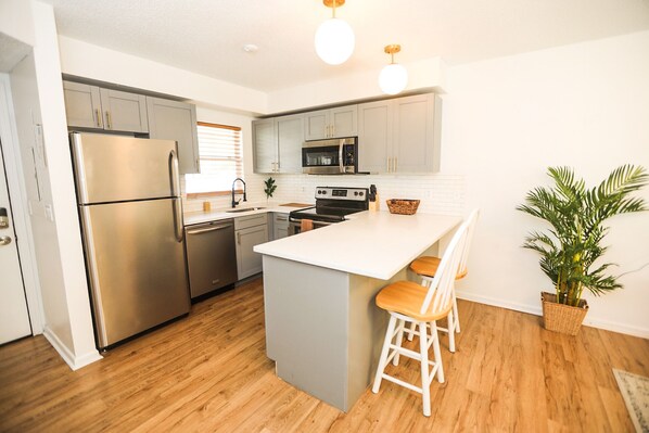 A modern kitchen with stainless steel appliances, a white island with bar stools, and a potted plant. - NEWLY RENOVATED SOPHISTICATED INDUSTRIAL TOWN HOME (St. Petersburg)