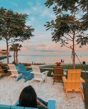 A beachside seating area with Adirondack chairs and a swing chair, overlooking the ocean with sailboats in the distance. - NEWLY RENOVATED SOPHISTICATED INDUSTRIAL TOWN HOME (St. Petersburg)