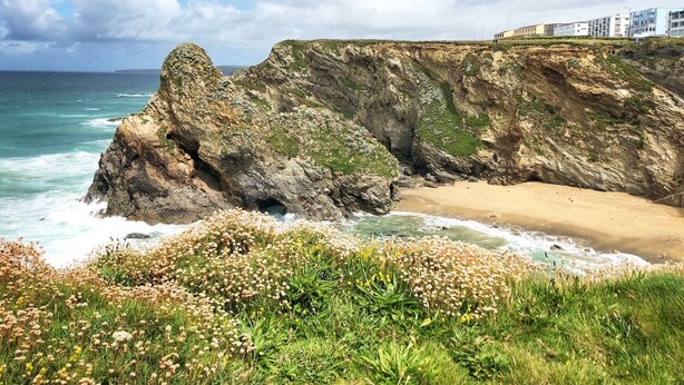 Un paysage côtier avec une falaise rocheuse, une plage et une rangée de bâtiments en arrière-plan.