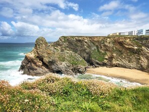 Un paisaje costero con un acantilado rocoso, una playa y una hilera de edificios al fondo.